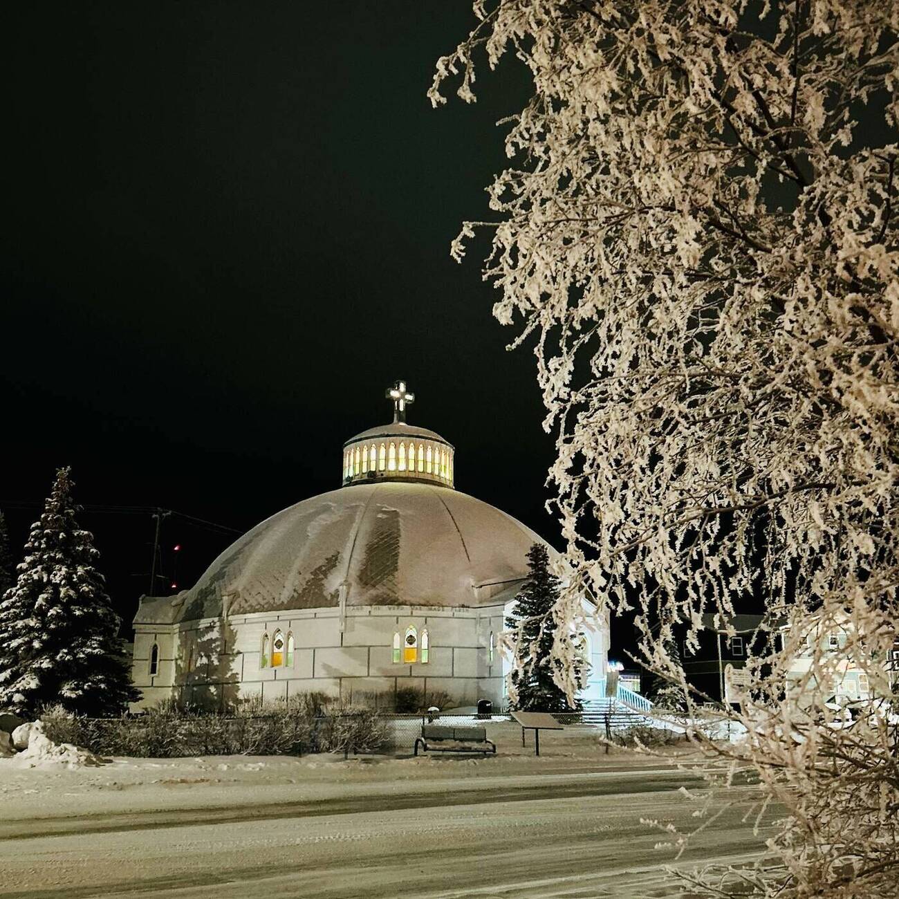 The Igloo Church of Inuvik glowing at night among hoarfrost-covered trees